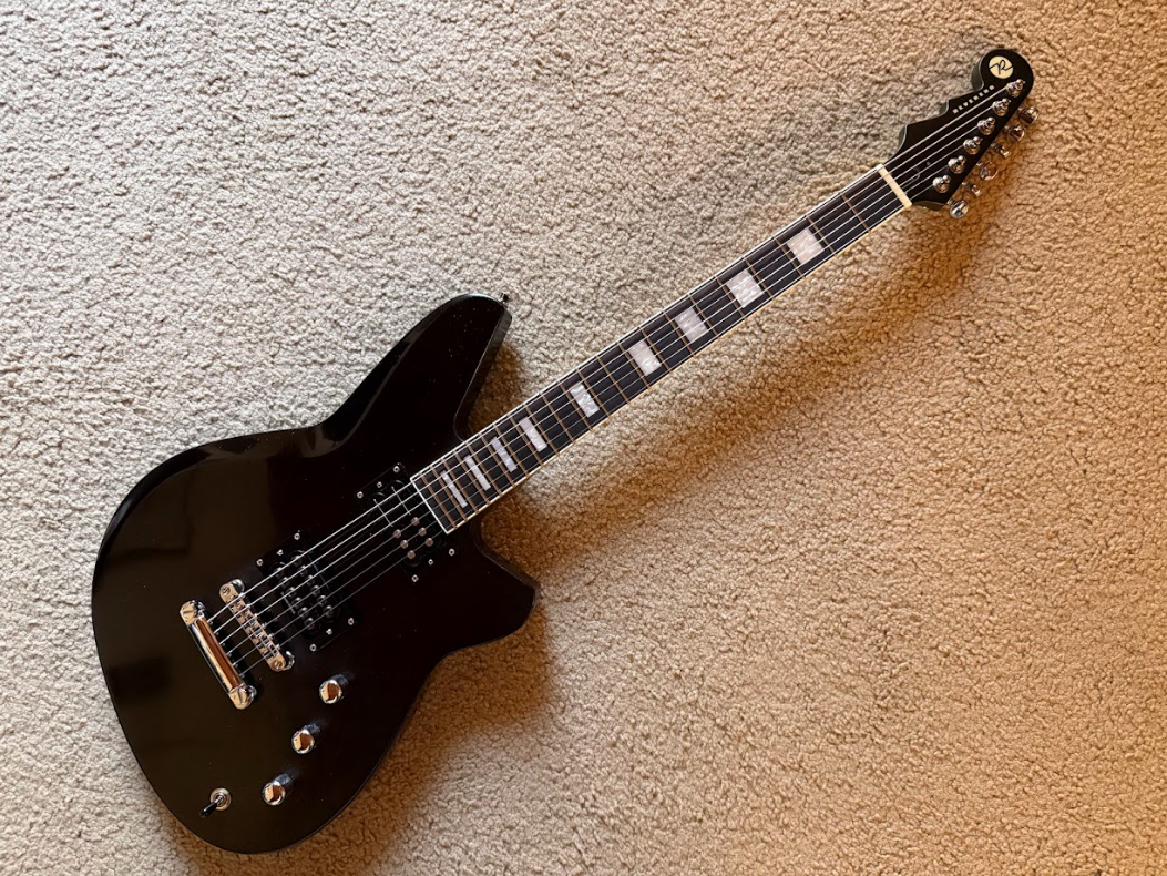 Black electric guitar lying on a beige carpet.