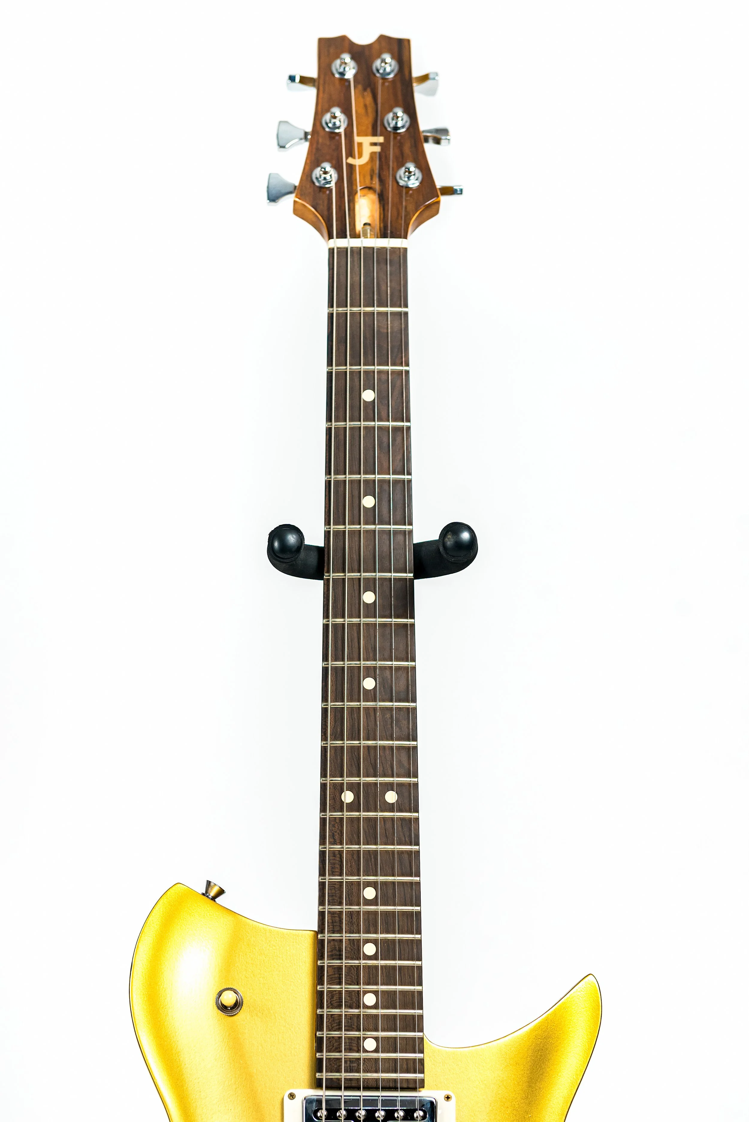 A yellow electric guitar hanging on a white wall.