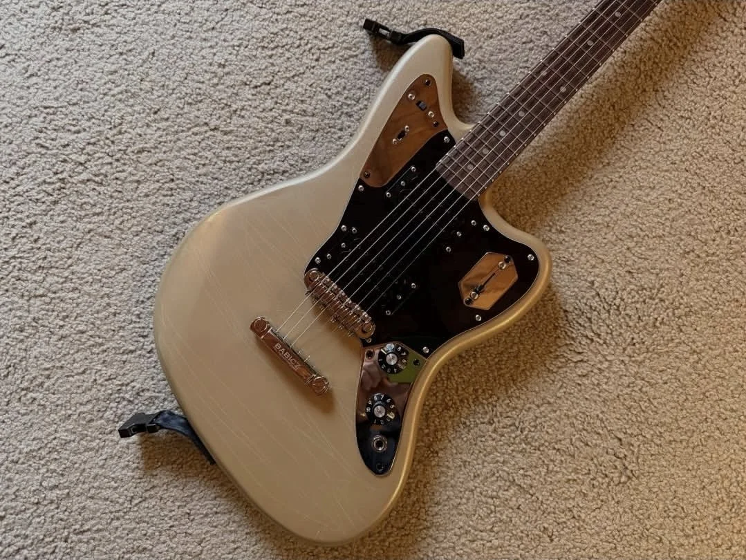 Cream-colored electric guitar with black pickguard, wooden pickup covers, and multiple control knobs, resting on a beige carpet.