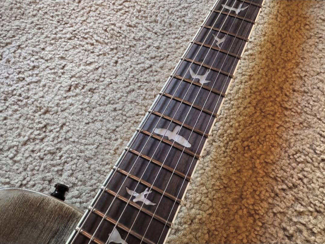 Close-up of a guitar neck with star-shaped and other patterned fret markers, lying on a carpeted floor.