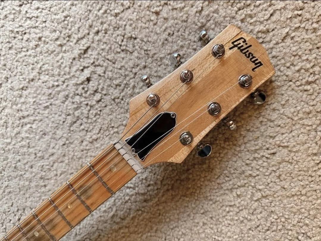 Close-up of a Gibson branded electric guitar headstock with tuning pegs and strings, resting on a beige carpet.