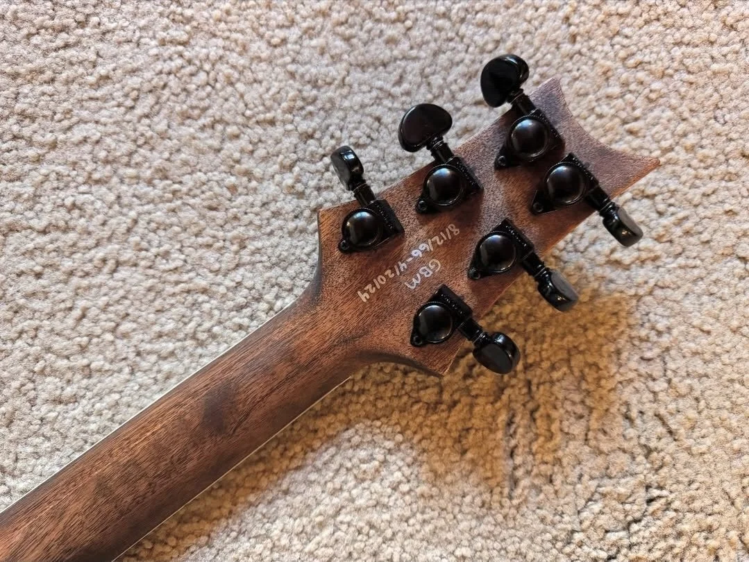 The back of a guitar headstock with six tuning pegs on a beige carpet.
