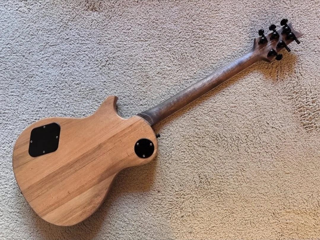 An electric guitar with a natural wood finish, laying on a beige carpet.