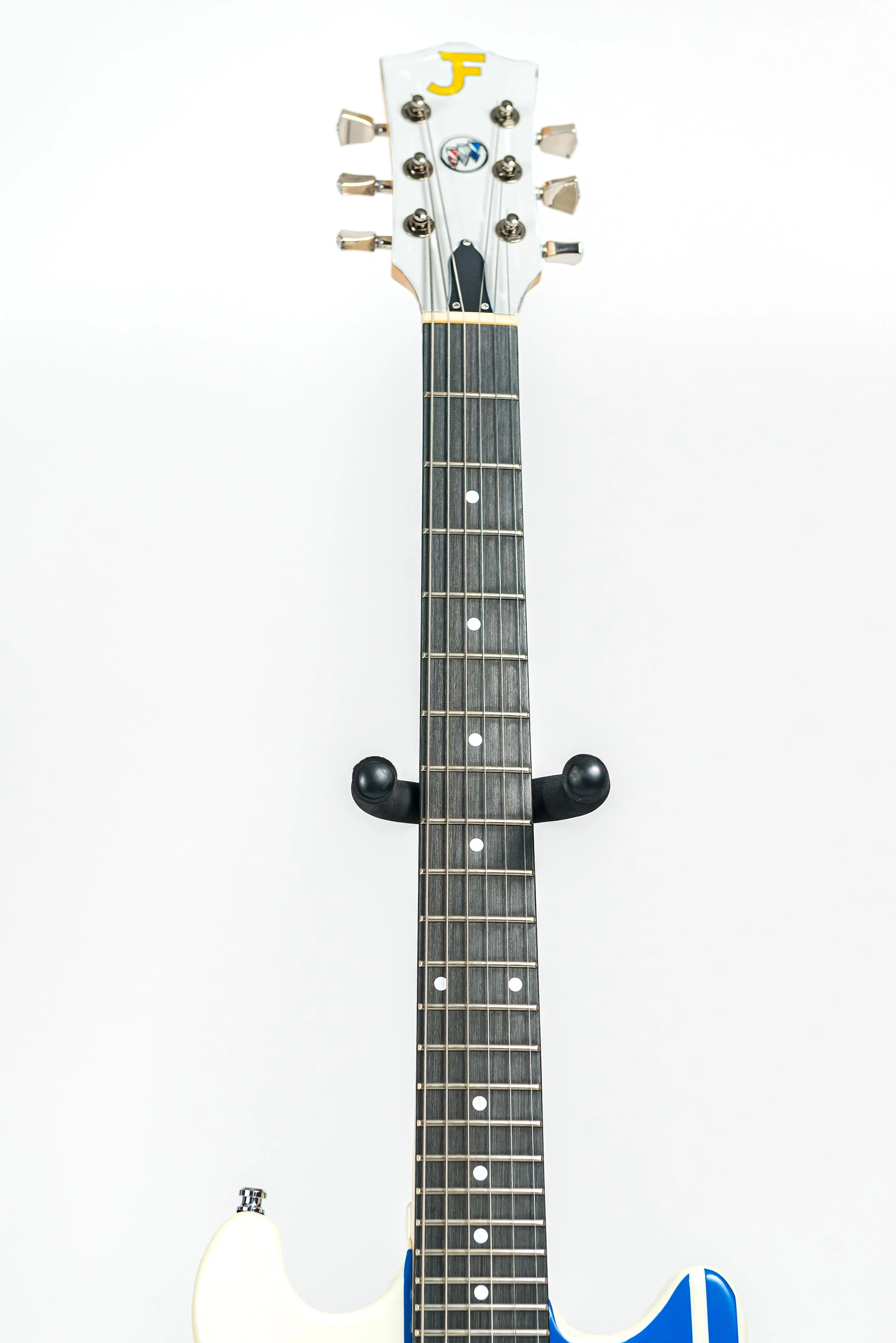 Close-up of the headstock and neck of an electric guitar mounted on a wall against a white background.