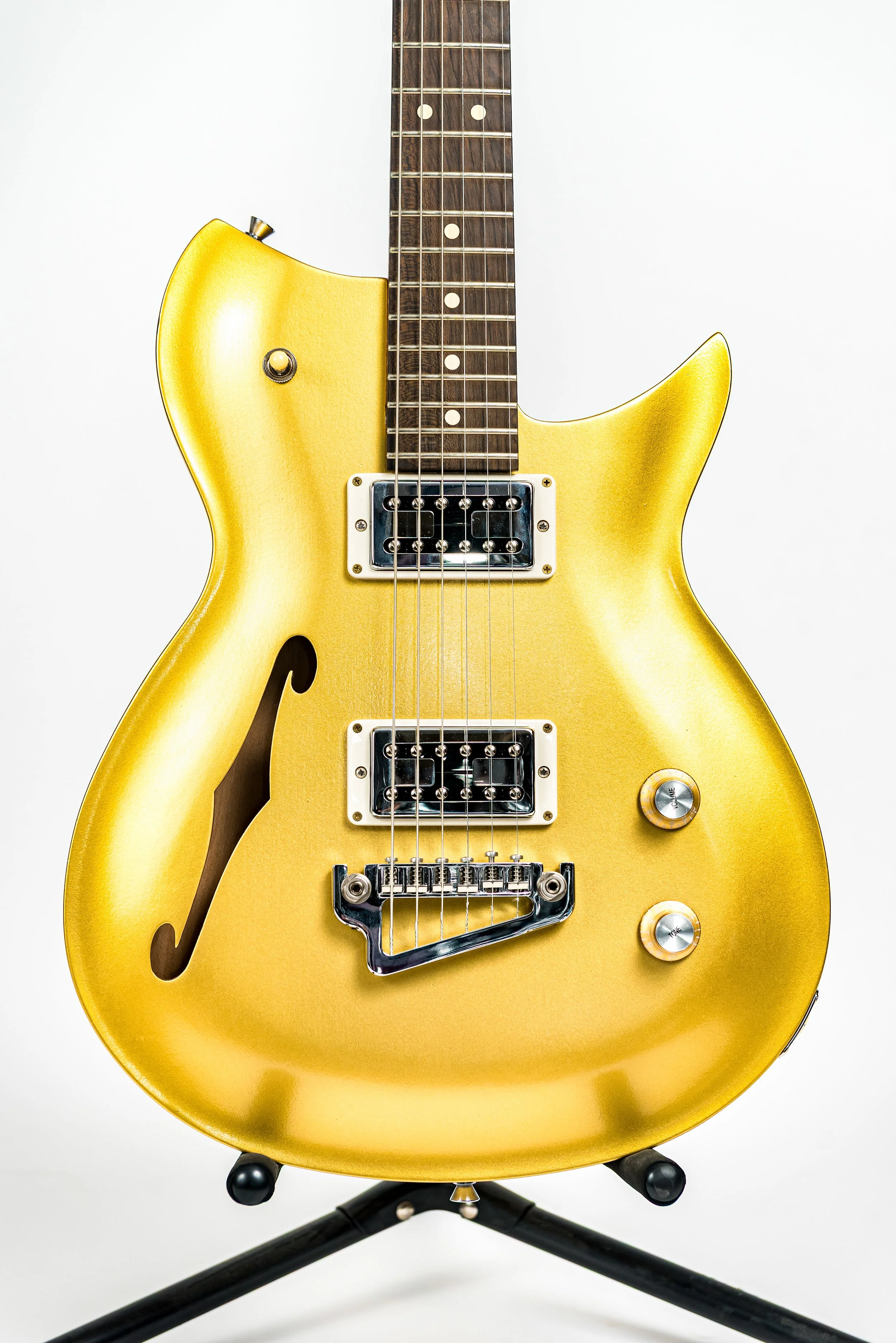 A yellow electric guitar with dual pickups on a black stand against a white background.