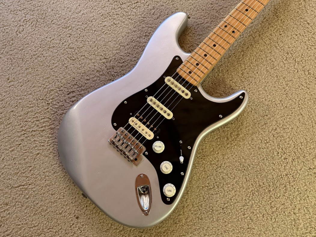 Silver electric guitar with a black pickguard resting on a beige carpet.