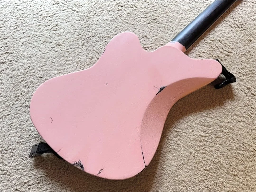 Pink toy guitar lying on beige carpet with black accents and a black neck.