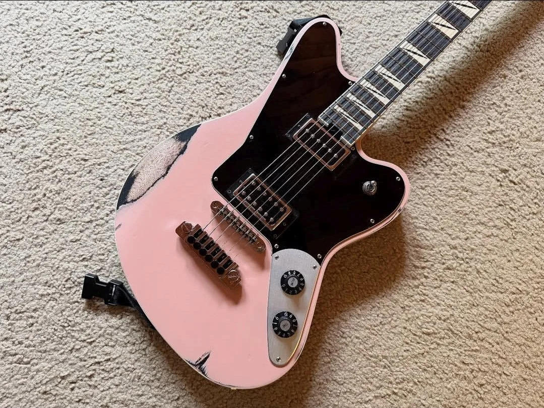 Pink electric guitar with black pickguard and control knobs, placed on a beige carpet.