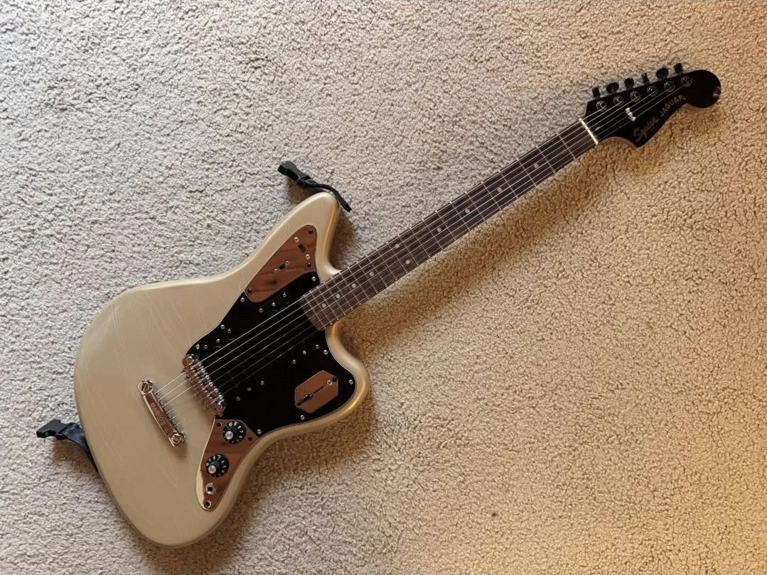 Cream-colored electric guitar with black pickguard and brown accents on a beige carpet.