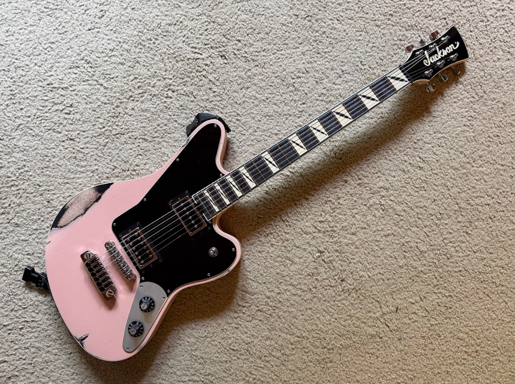 Pink and black electric guitar on a beige carpet.