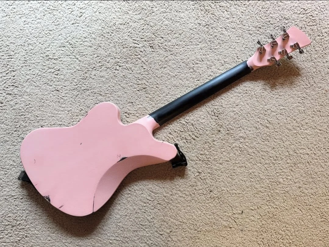 A pink toy guitar with black tuning pegs resting on a beige carpet.