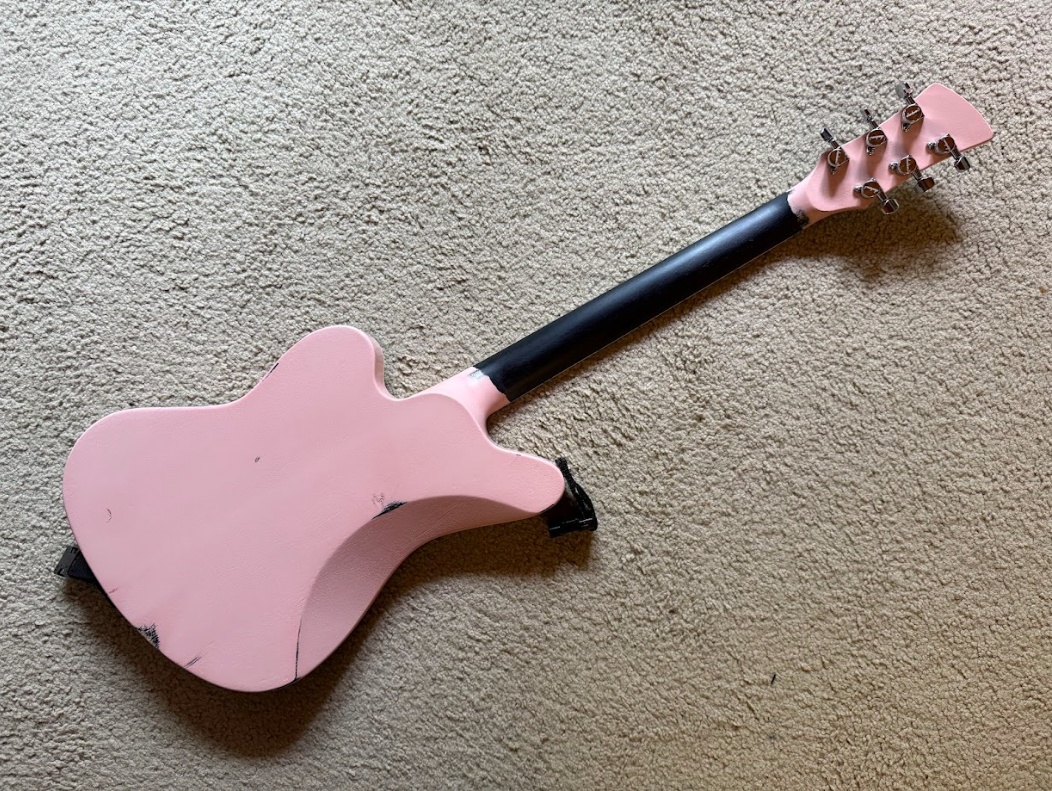A pink toy guitar lying on a beige carpet.