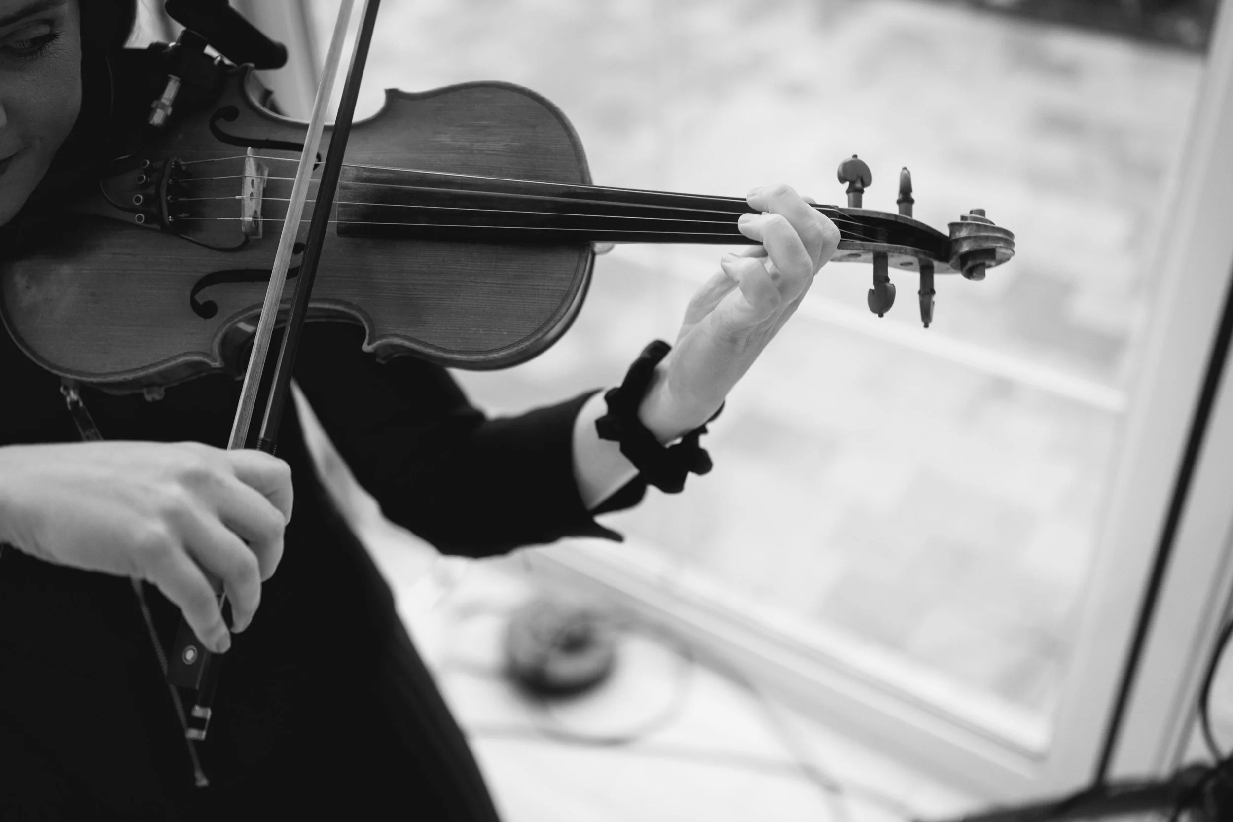 A wedding violinist, focusing on their hands and the instrument, with a bow in one hand and the violin in the other.