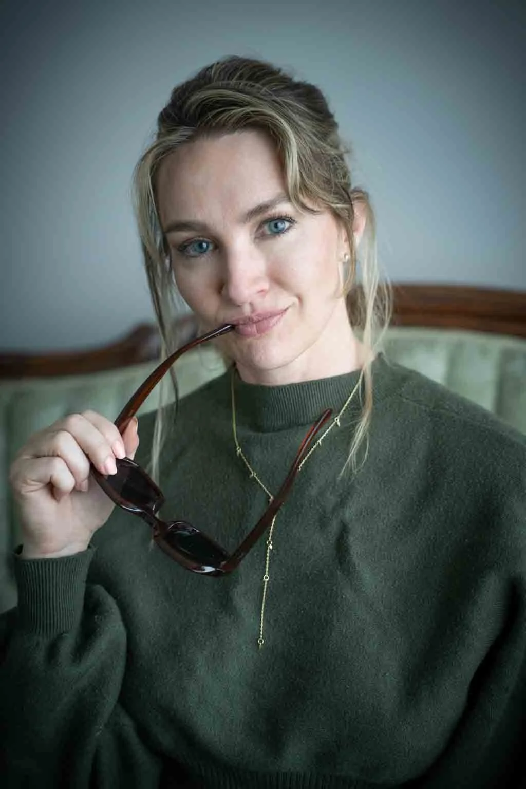 Minette Martin - Close-up portrait of a woman with long wavy hair and blue eyes, wearing a gold necklace, looking directly at the camera.