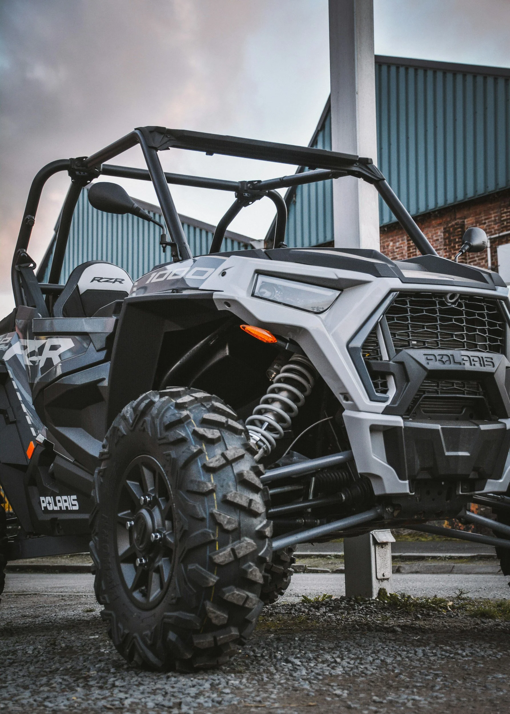 Off-road Polaris RZR vehicle parked outdoors near a building with blue siding and brick.