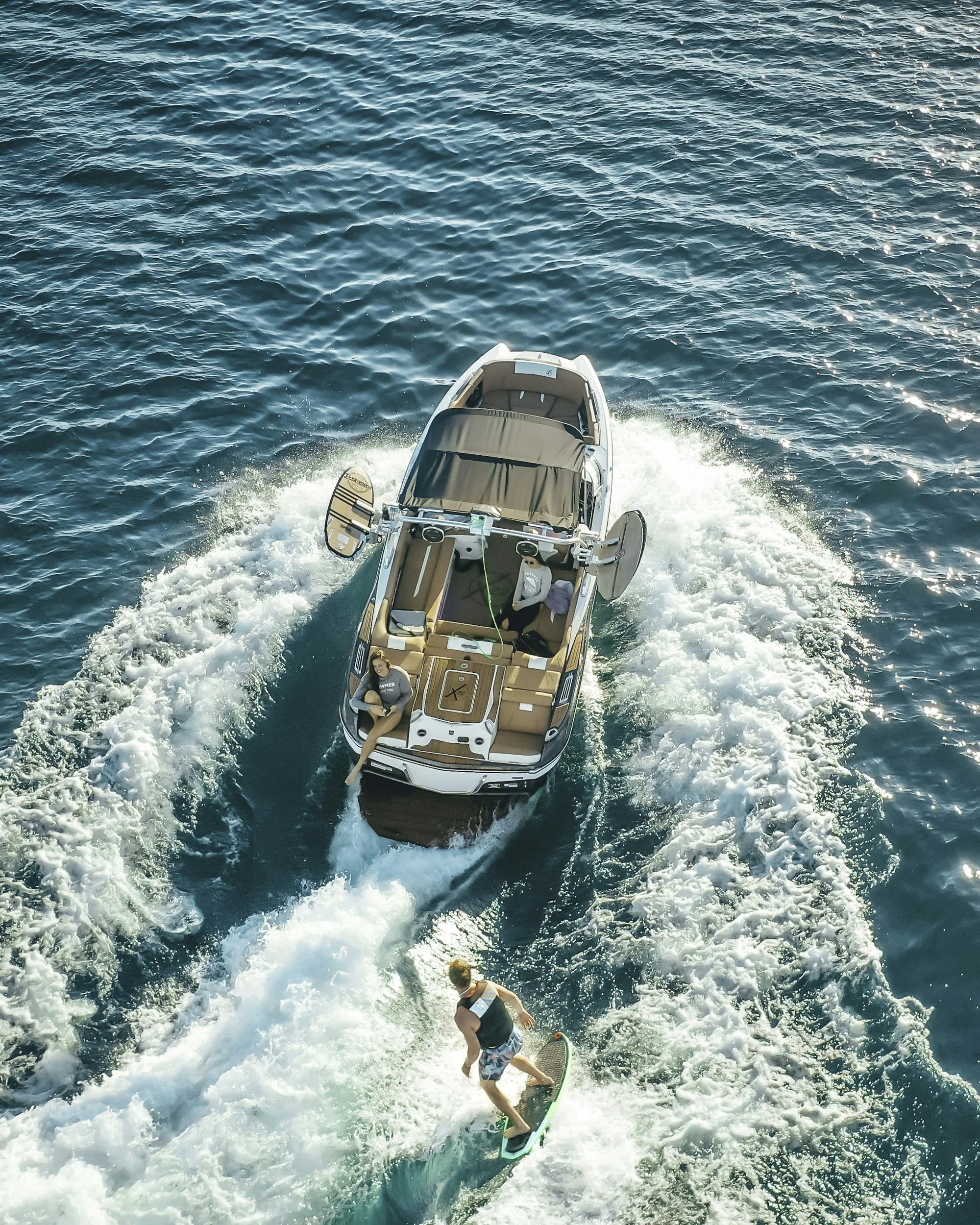 A boat with two people on board being used for wakeboarding on the water, while a man is wakeboarding behind the boat.