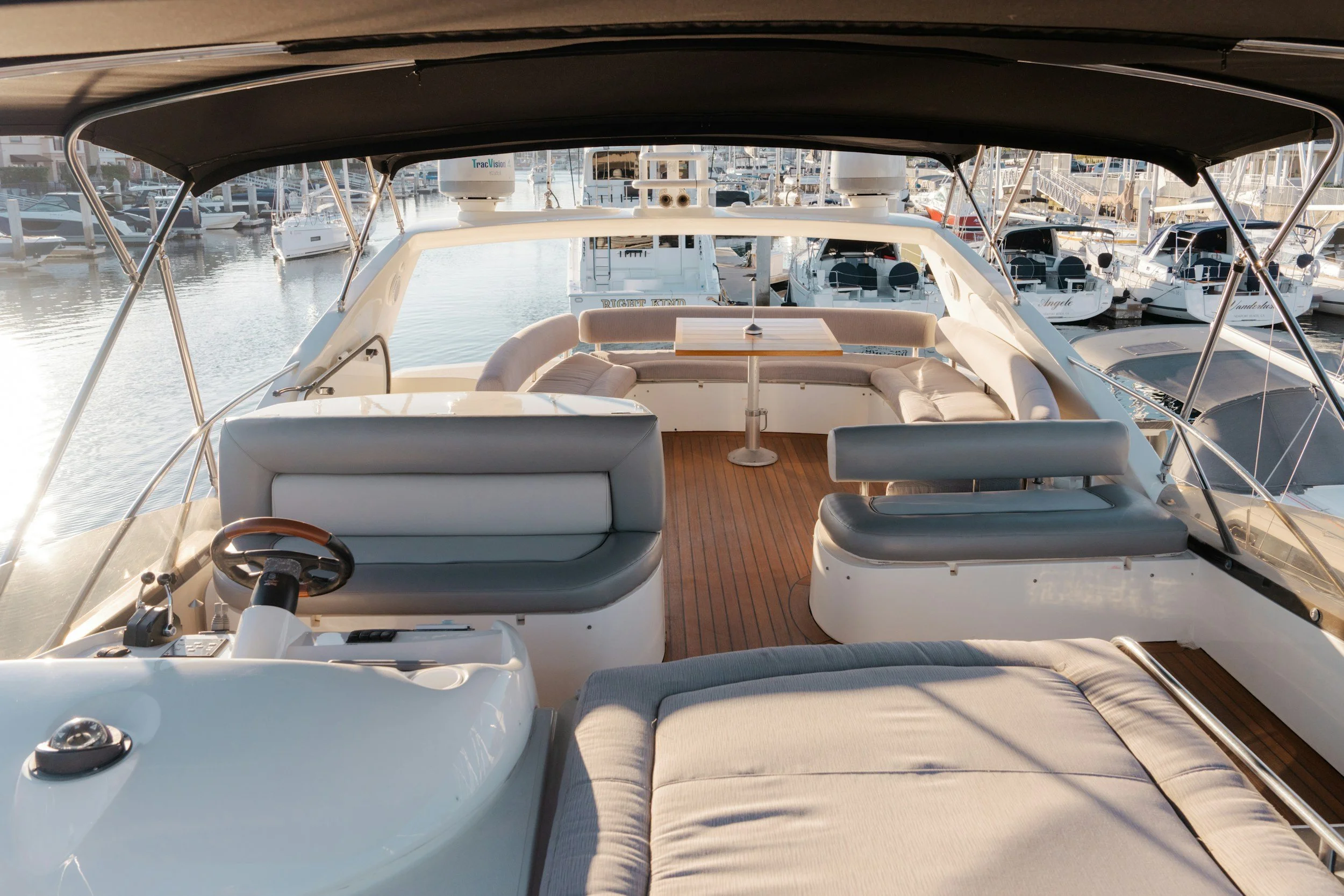 Upper deck of a yacht docked at a marina with boat seating, a table, and view of other boats in the background.