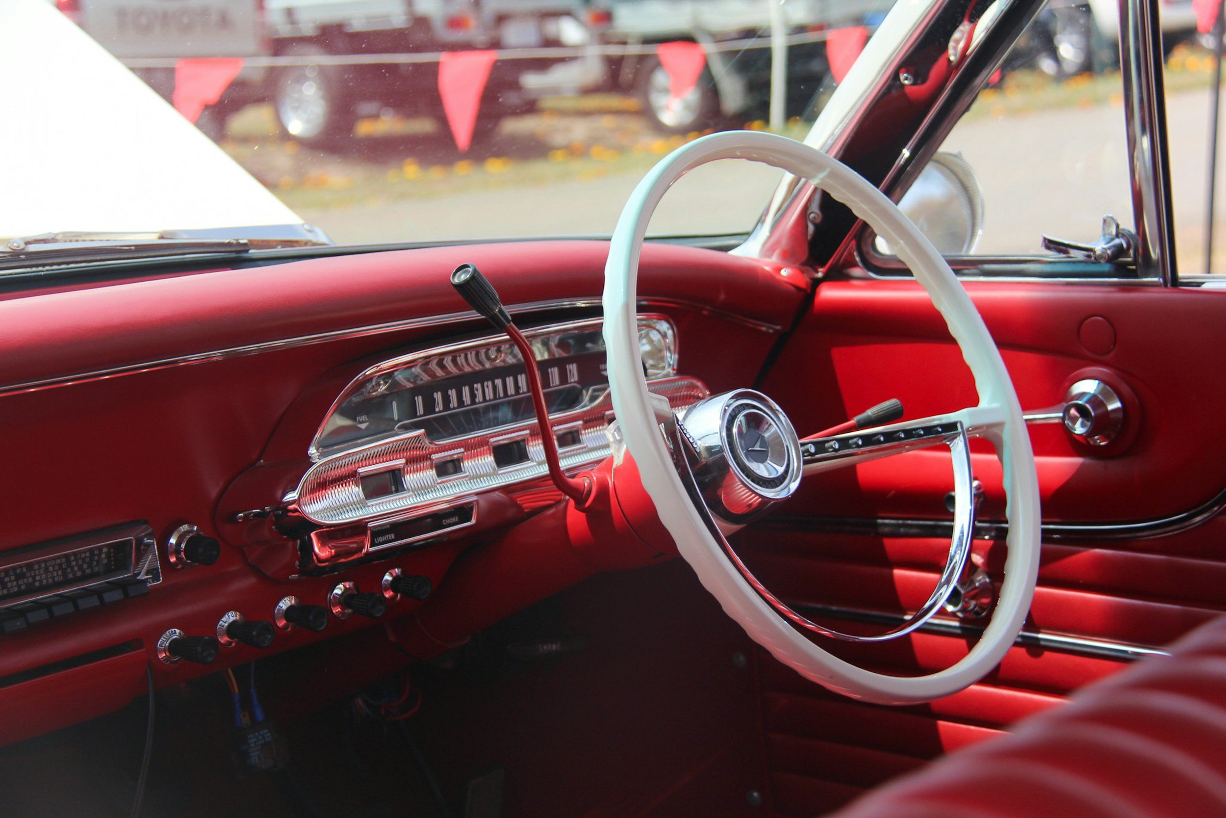Interior of a vintage red car showing the steering wheel, dashboard, and gear shifter.