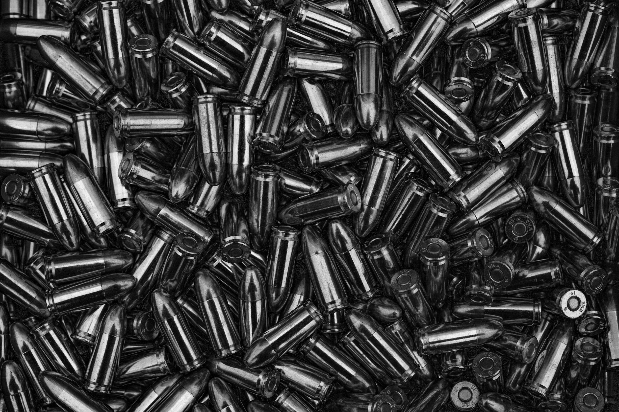 A large pile of metallic bullet casings, mostly shiny and reflective, in a monochrome color scheme.