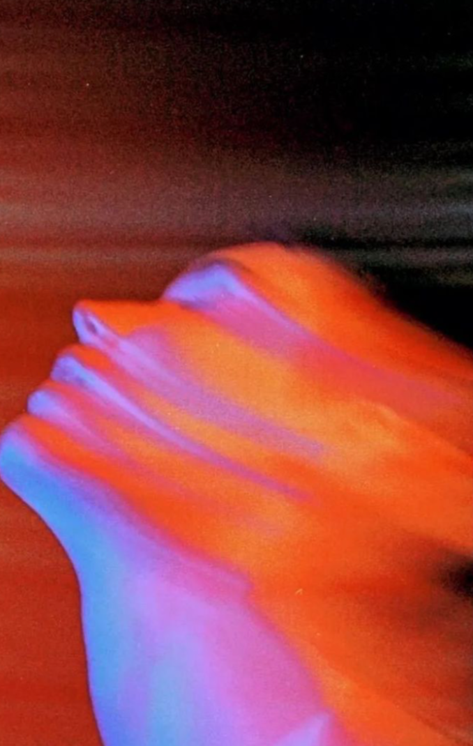 Une main levée sous une lumière colorée en dégradé de violet, orange et rouge, avec un fond sombre.