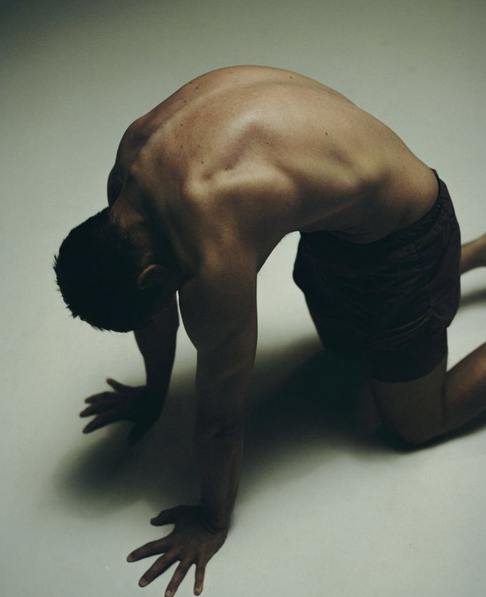 Un homme semi-nu est à genoux sur le sol, le dos arrondi, dans une posture de d'étirement pilates
