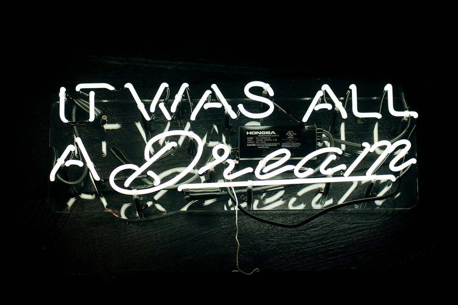 Neon sign with the words "It Was All a Dream" in white letters, mounted on a dark wall.
