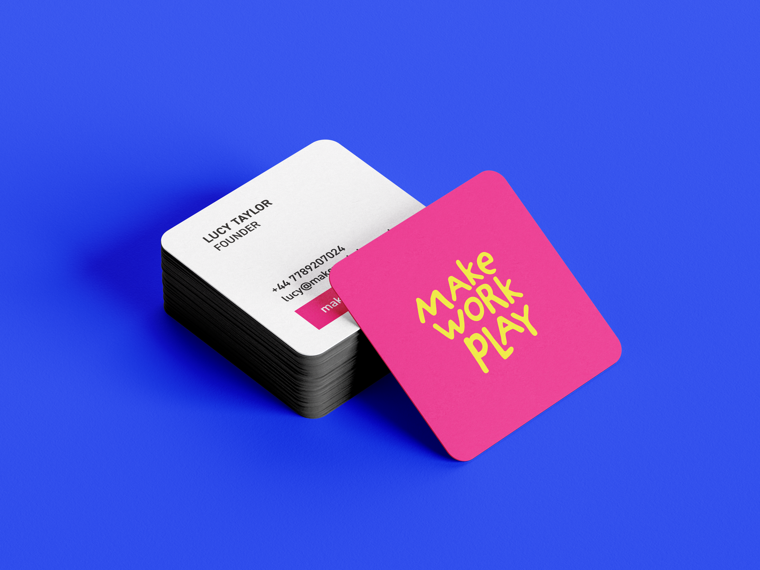 Stack of business cards on a blue background, one card reads 'LUCY TAYLOR, FOUNDER,' and another card that says 'MAKE WORK PLAY' in yellow text on a pink background.