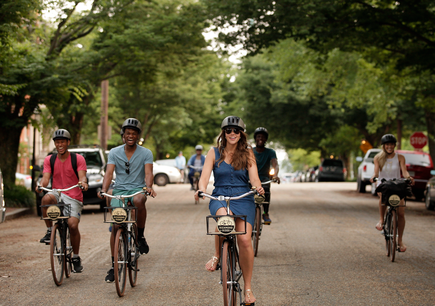 Group of people riding bikes on a tree-lined street, smiling and enjoying a sunny day.