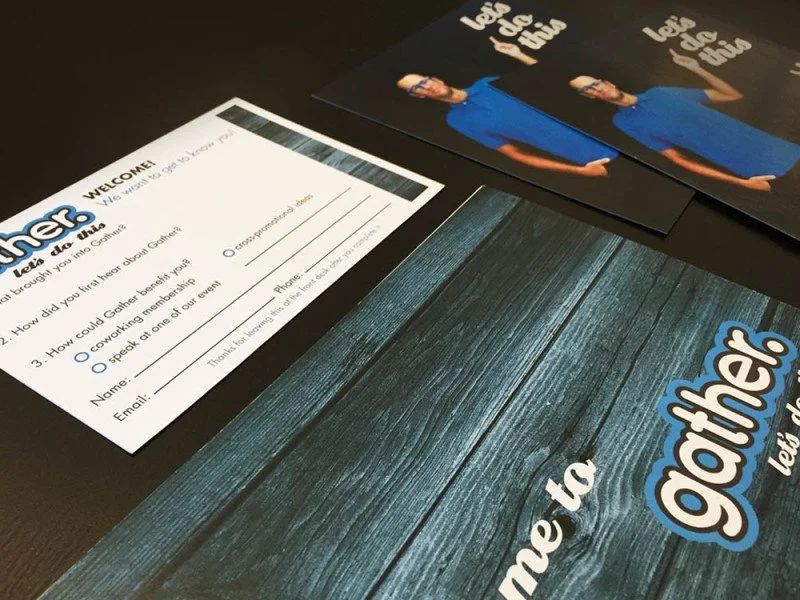 Event registration forms and promotional materials on a black table, including a white sign-up sheet and flyers with a woman in a blue dress.