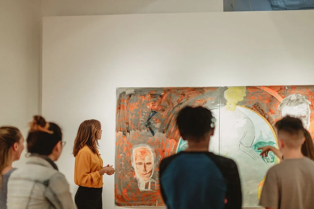 A group of people observing a mixed media artwork in an art gallery, featuring a woman's face, abstract shapes, and vibrant colors.