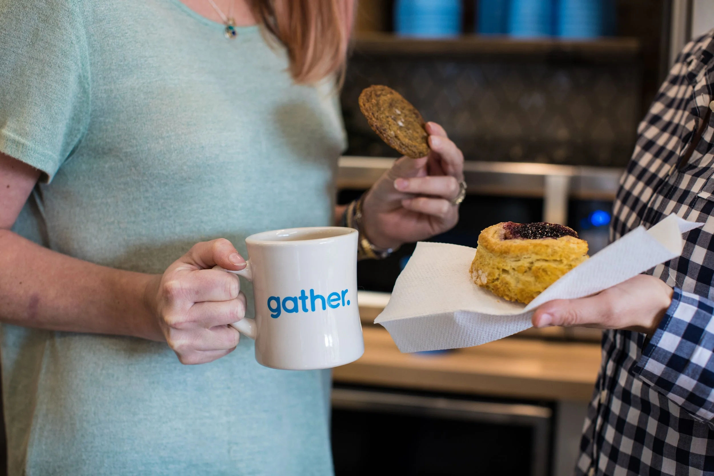 A person in a green shirt is holding a white mug with the word 'gather' on it, and another person in a checkered shirt is holding a plate with a slice of cake. Another hand with a cookie is visible near the cake.
