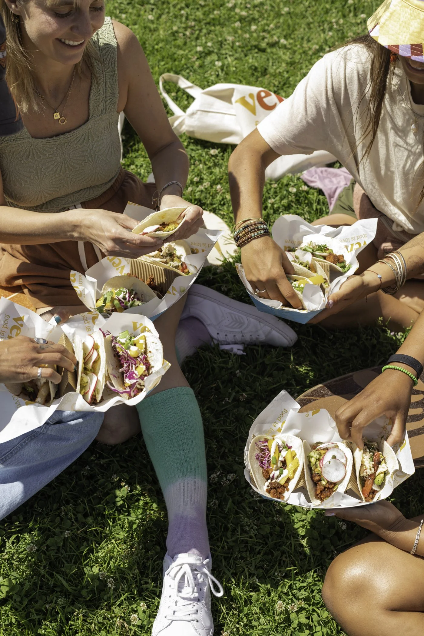 People sitting on grass having a picnic with paper food containers filled with tacos and salads.