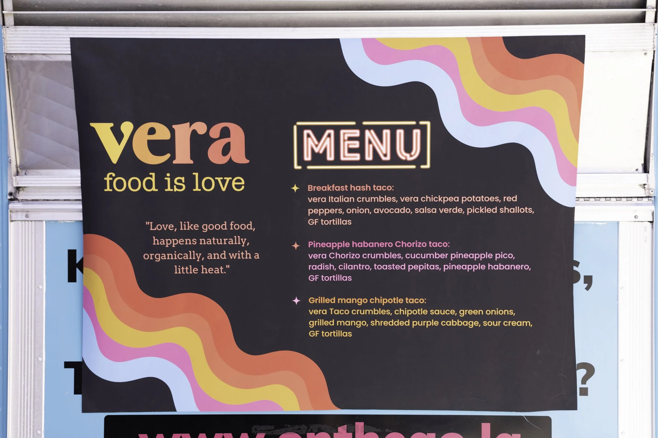 A colorful menu board with a black background and bright, wavy designs in blue, pink, yellow, and orange. The board features the name 'vera' in large yellow-orange text, followed by the phrase 'food is love' and a quote about good food. The menu list