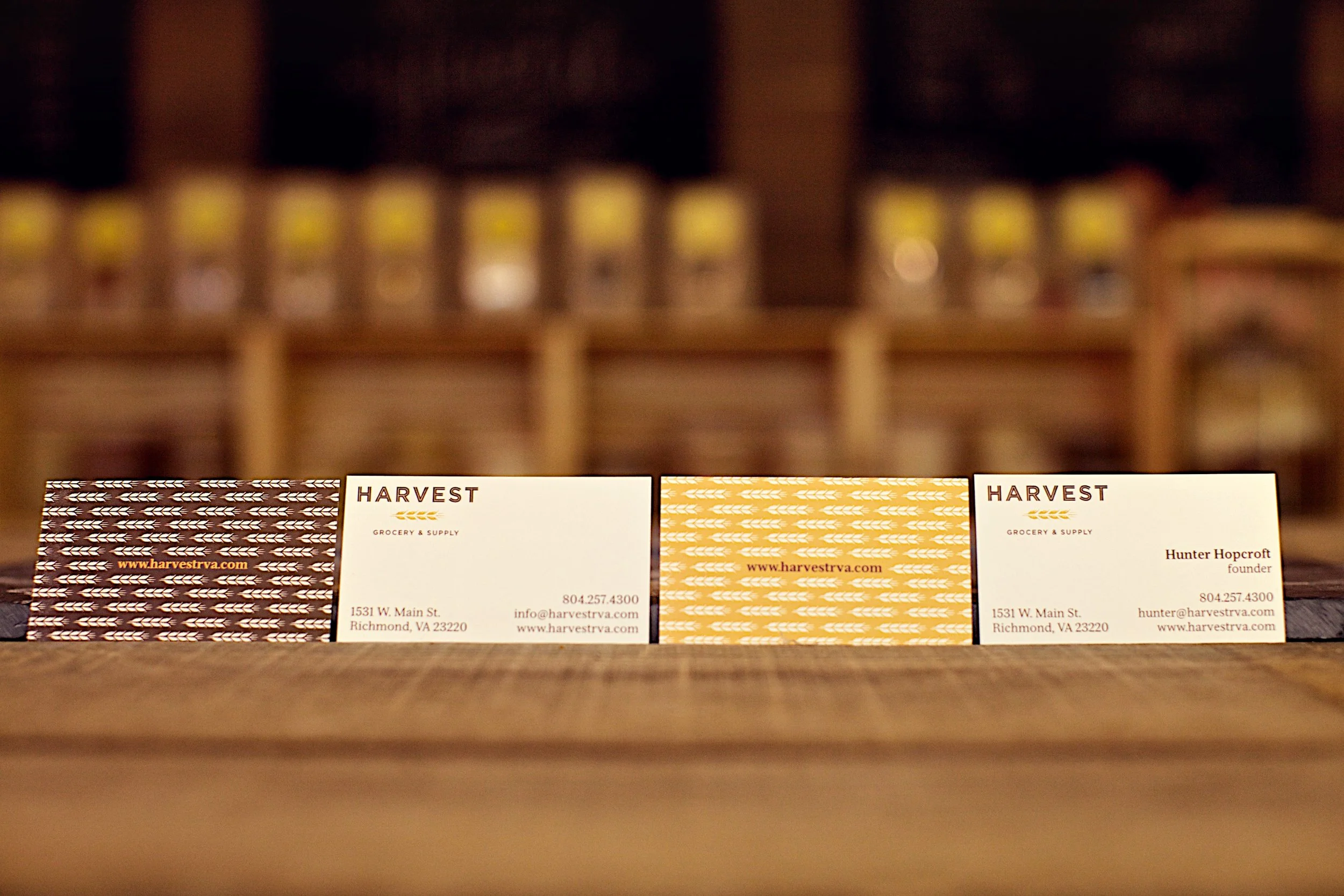 Business cards from Harvest Grocery & Supply displayed on a wooden surface, with a blurred background.