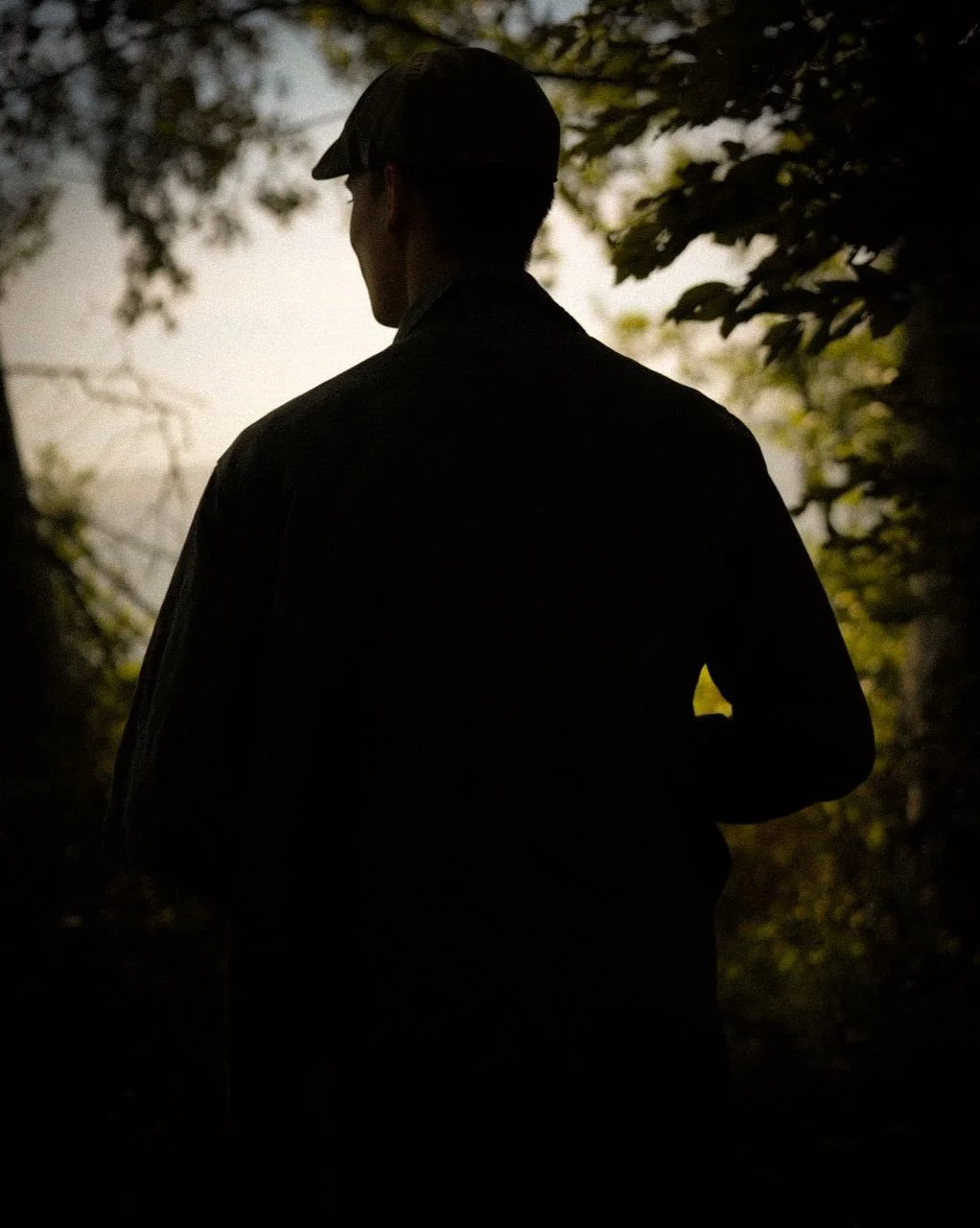 Silhouette of Sylvian Lèvin standing in nature, backlit by warm light and surrounded by trees.