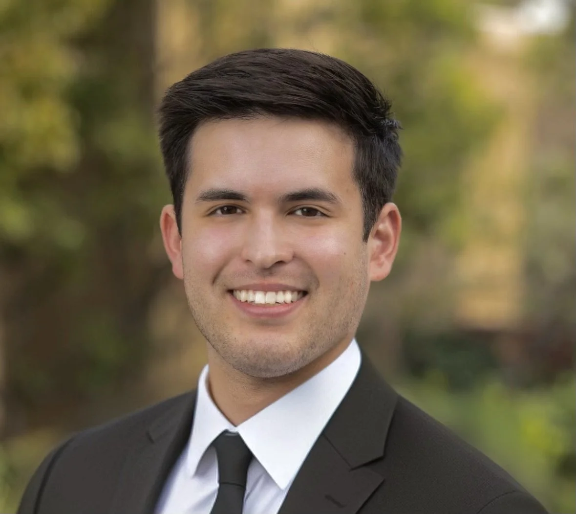Headshot of man with dark hair, dark suit, light collared shirt and dark tie.