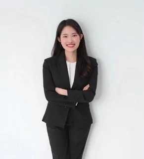 Woman standing in dark suit with white top. Long dark hair. Arms crossed.