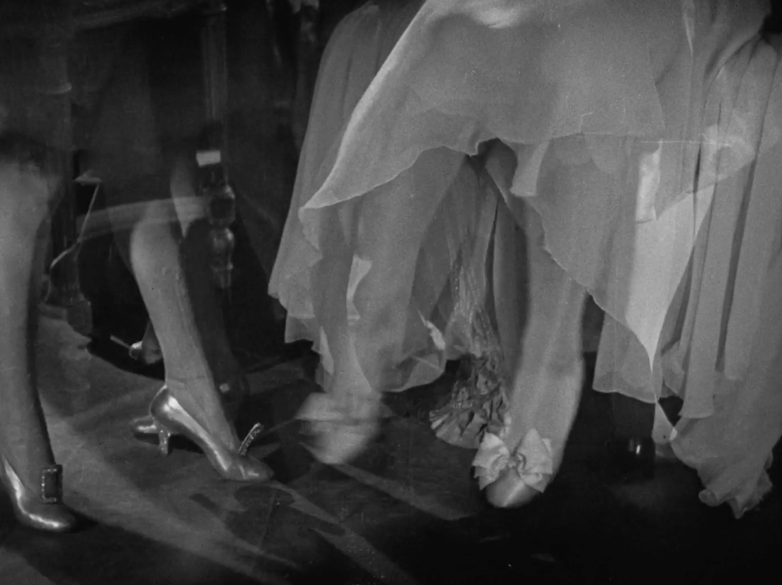 Black and white photo of a woman in vintage clothing, leaning into a car, wearing high heels and a dress with a big bow, with her face partially visible.