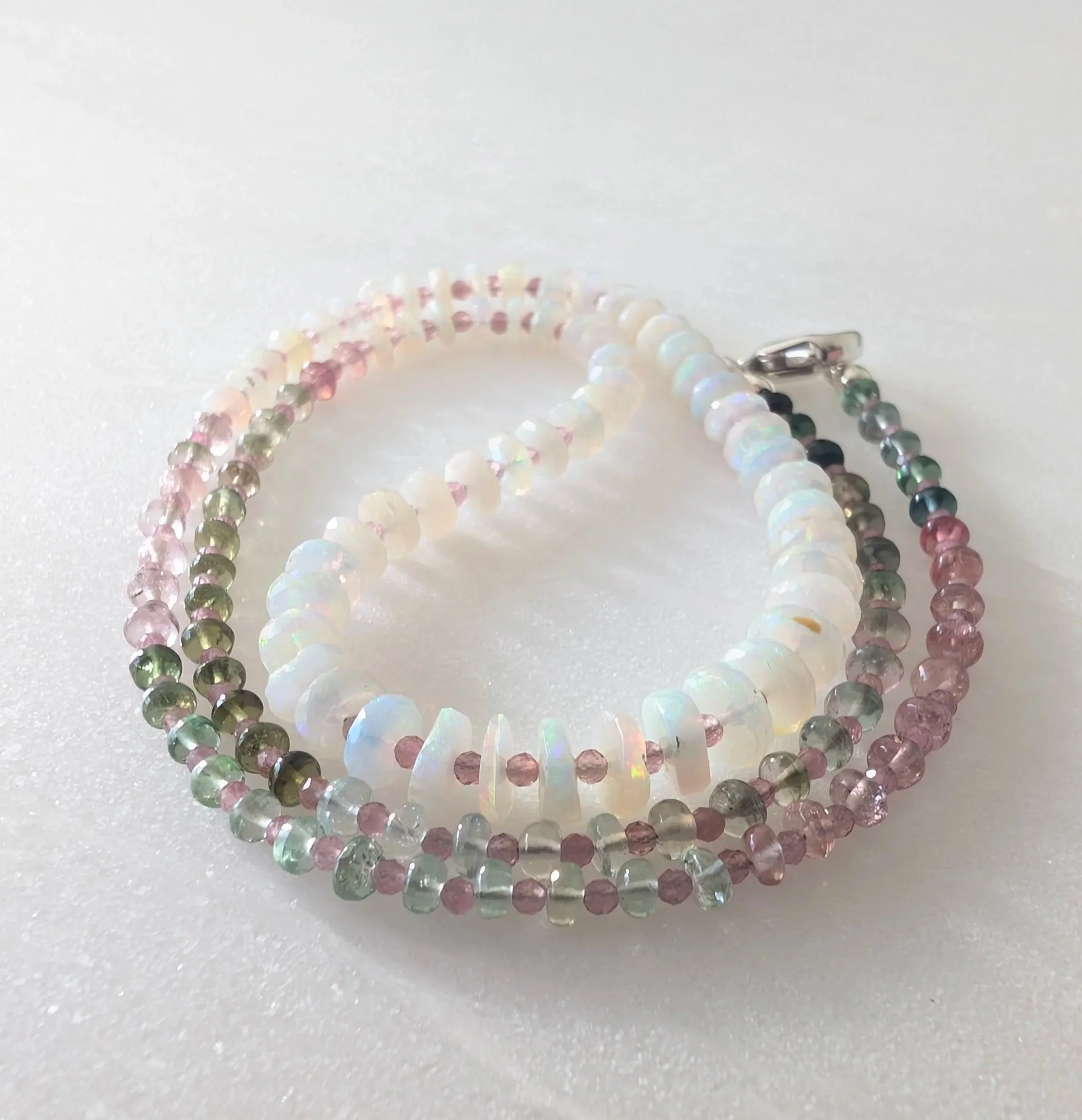 Two beaded bracelets, one with pastel green and pink beads and the other with iridescent white beads, on a white surface.