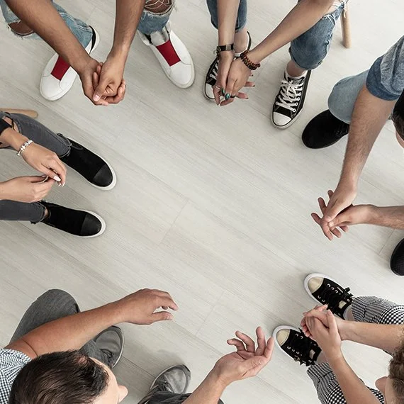 A group of people standing in a circle, holding hands, viewed from above.