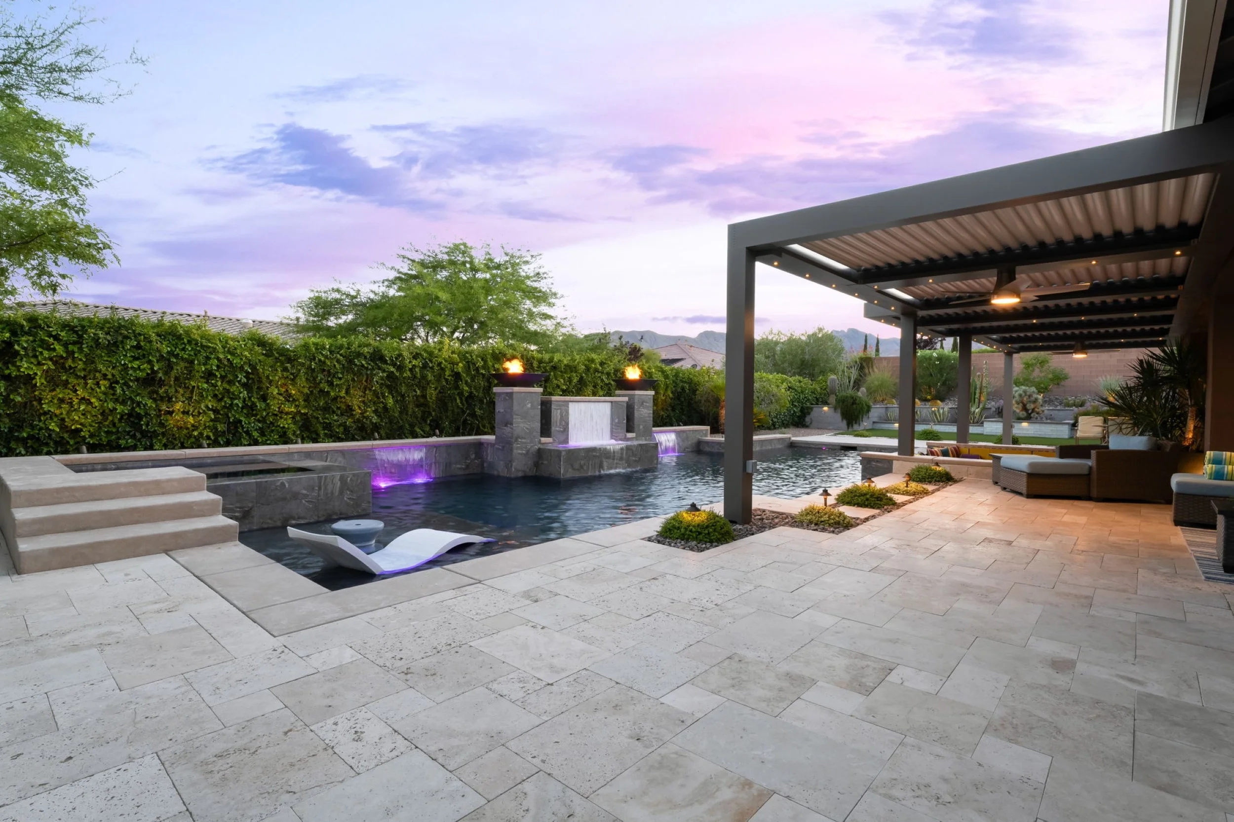 Backyard patio with swimming pool, stone steps, and outdoor seating area under a pergola, with mountain view and twilight sky.