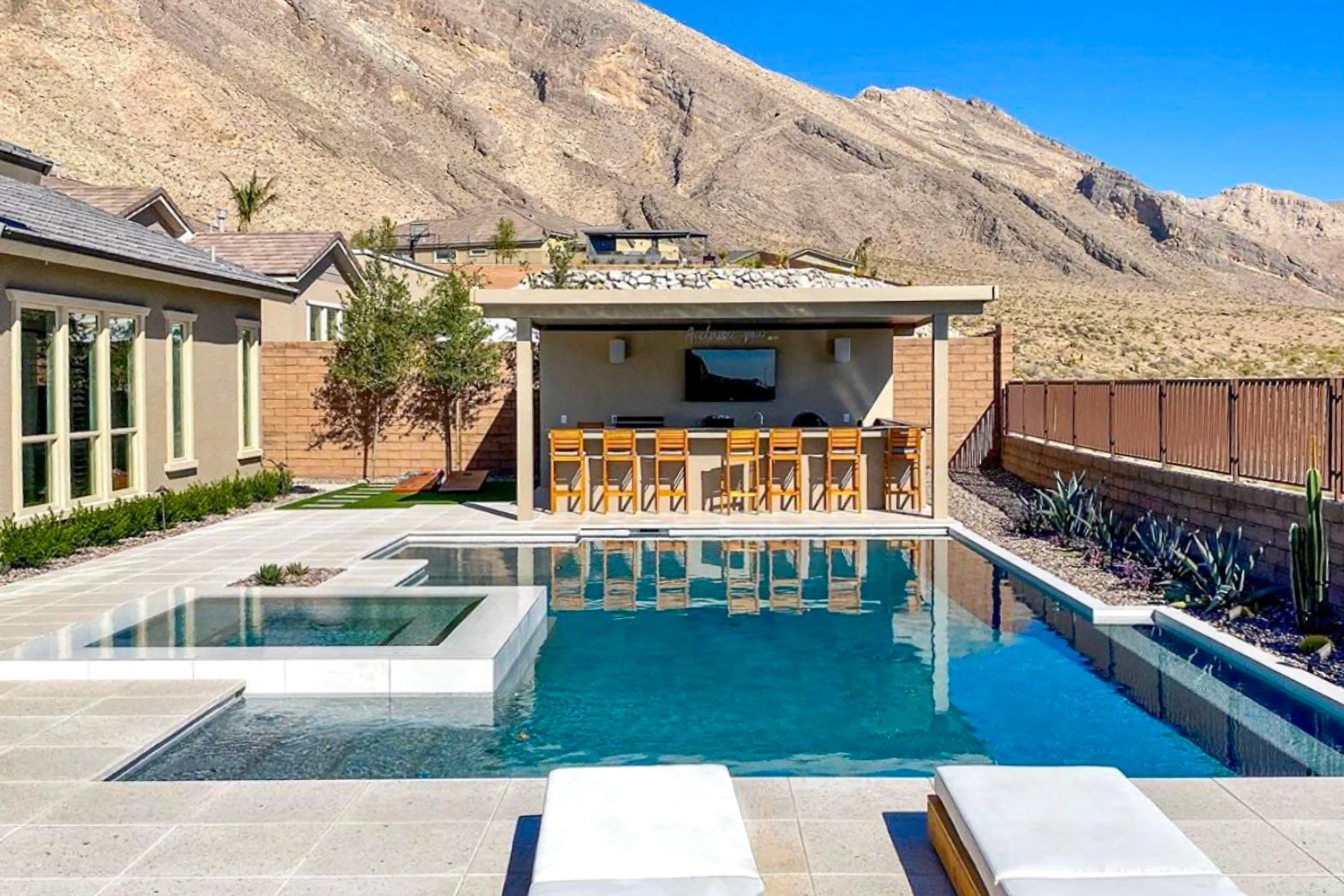 A modern white tile pool with patio cover pergola, media wall, outdoor tv with an infinity spa and paver decking, bbq area and outdoor kitchen with bar 