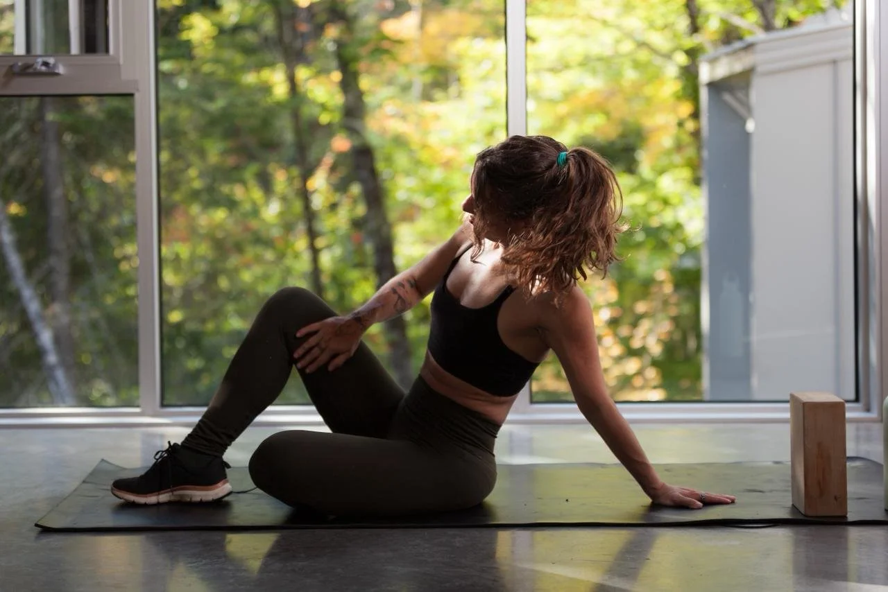 Woman practicing yoga on a mat indoors near large window with a view of trees outside.