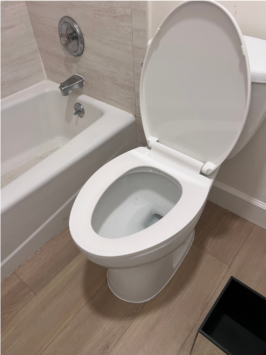 A Chavez Plumbing technician kneels in a modern bathroom while repairing a toilet, with tools laid out on the floor and a company van visible through the window.