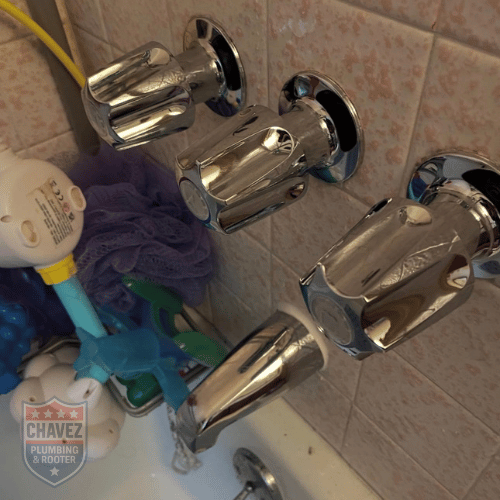 Close-up of four chrome bathtub faucet handles mounted on a tiled wall, with cleaning supplies and a purple cloth nearby.