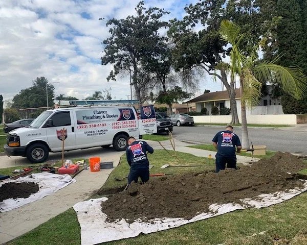 Plumber installing sewer line in a trench with a Chavez Plumbing van in the background