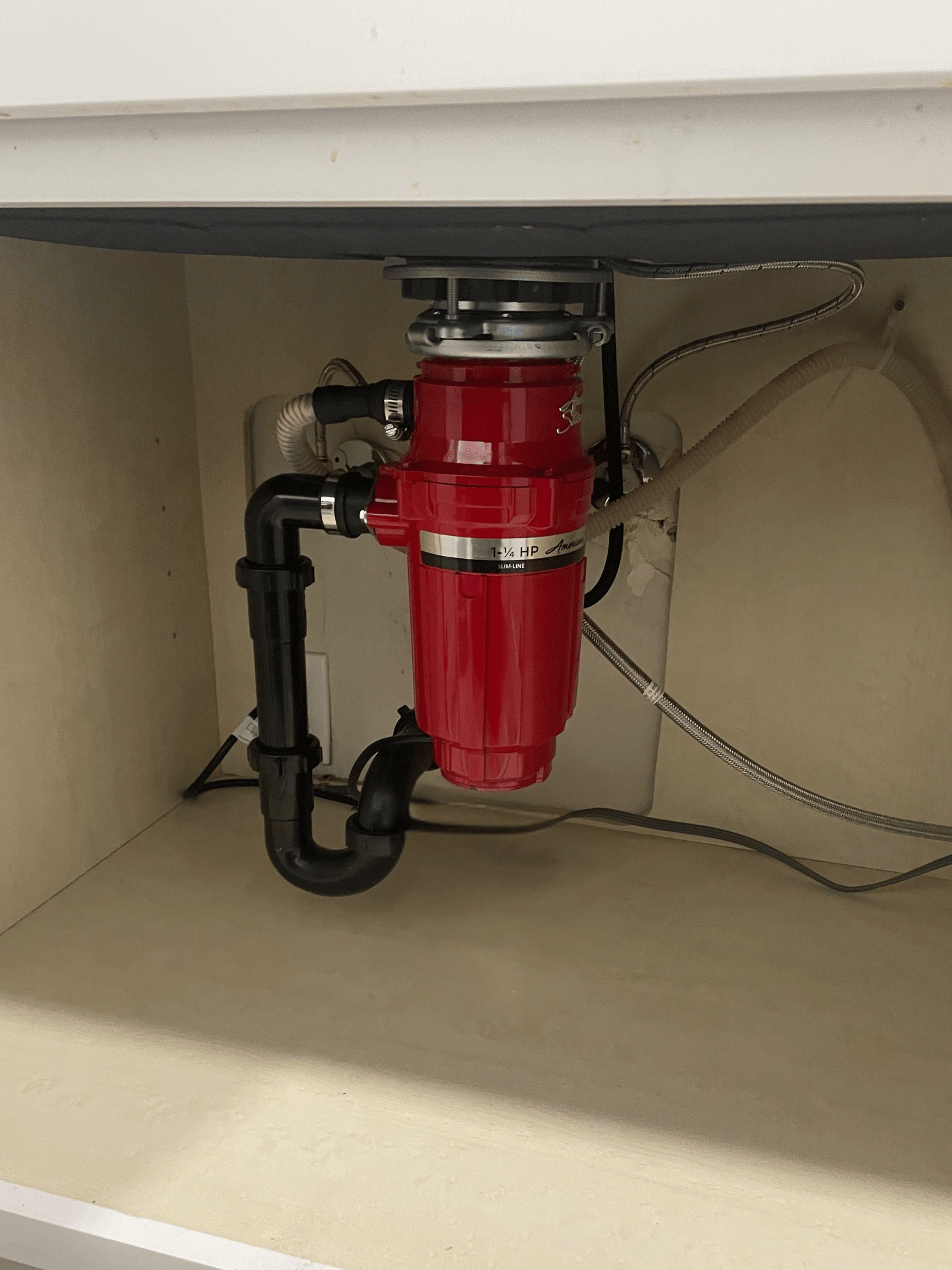 Chavez Plumbing technician installing a new garbage disposal under a modern kitchen sink, connecting plumbing and power lines with professional tools.