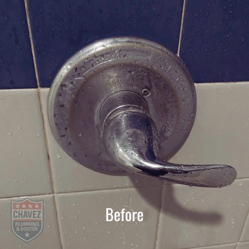 A close-up of a metal shower handle on a tiled bathroom wall, with water droplets on it and water around the base.