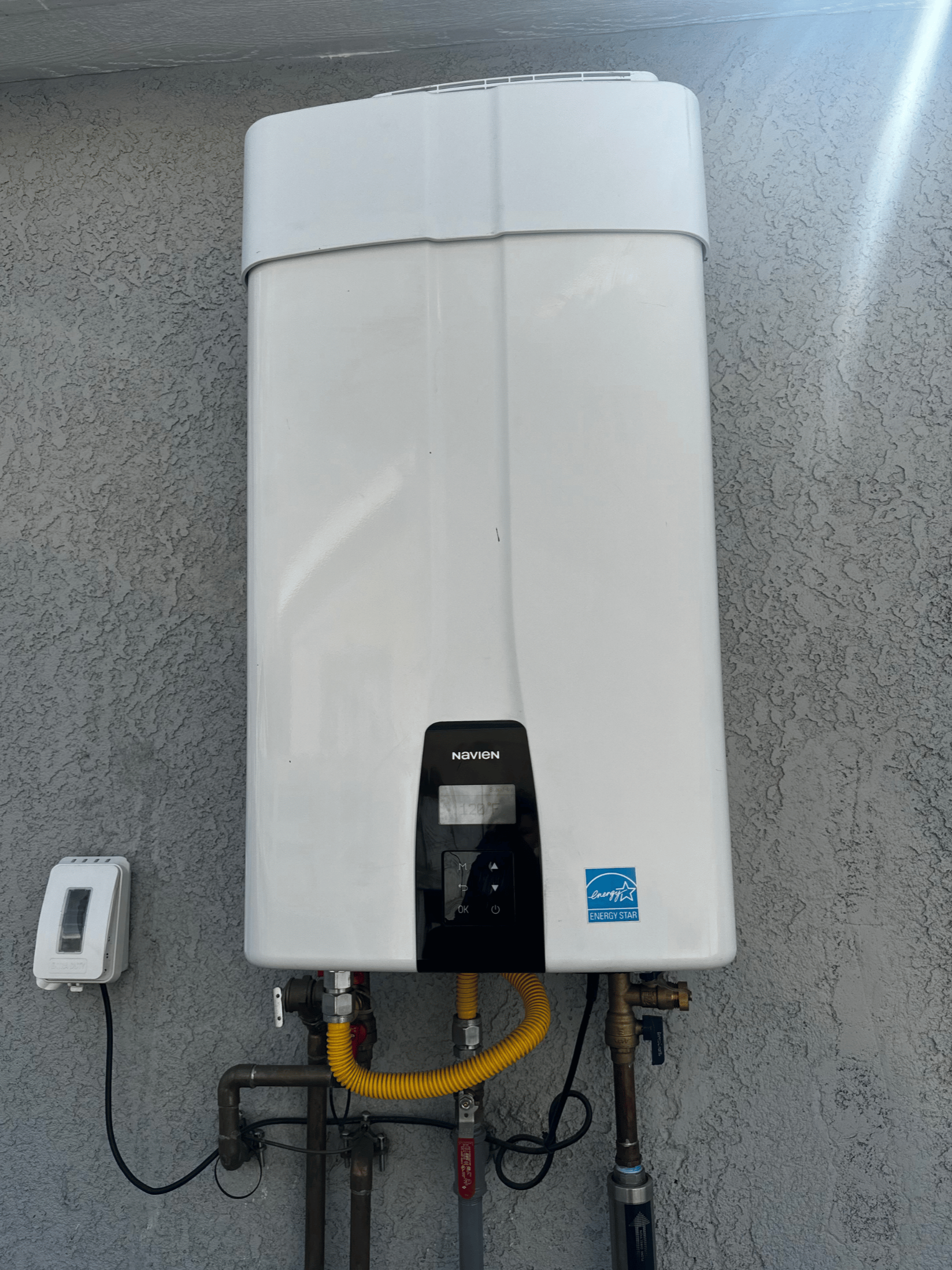 Chavez Plumbing technician servicing a tankless water heater, adjusting valves with tools inside a bright residential utility room.