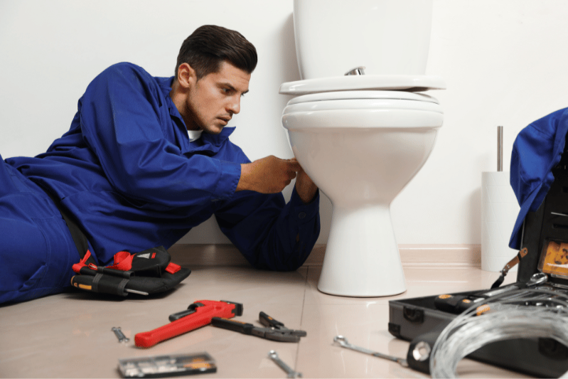 Technician repairing or installing a toilet using plumbing tools on the floor
